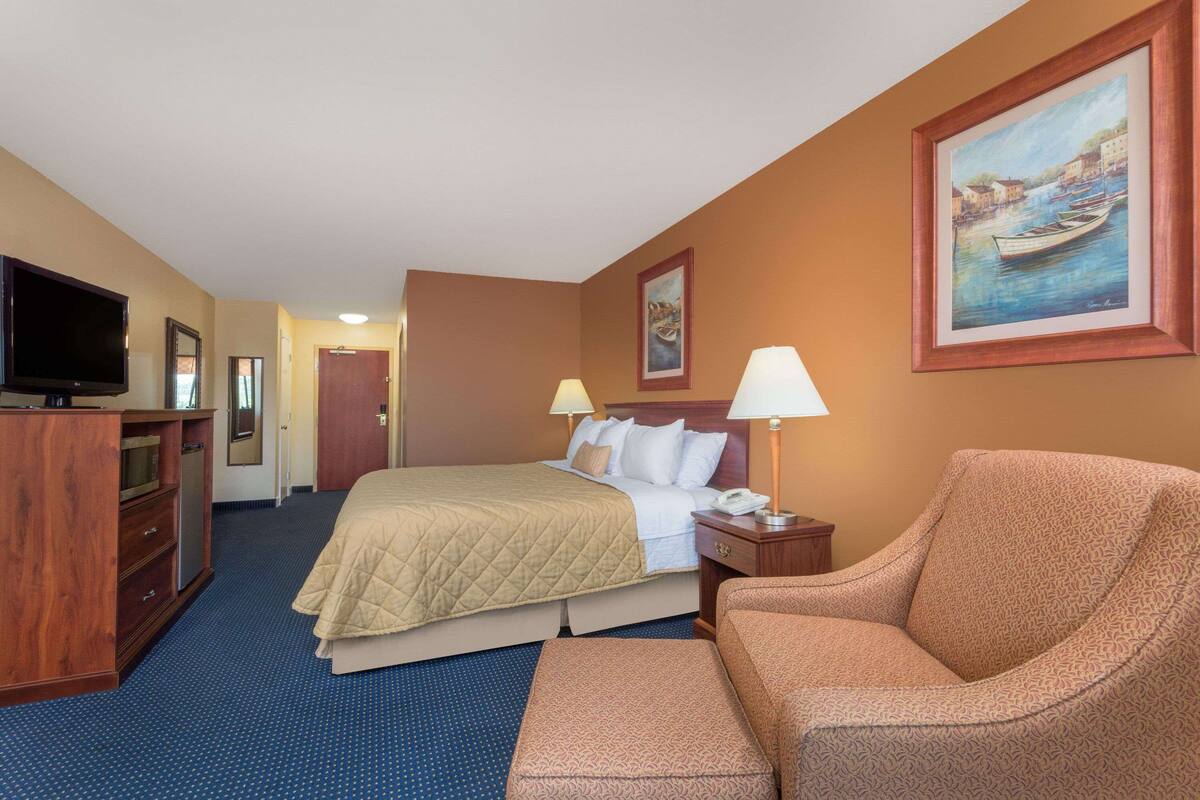 Een hotelkamer met een bed, een televisie, een bureau, een stoel en een schilderij aan de muur.