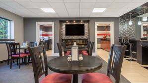 A dining area with a round table, chairs, a flat-screen TV, and a bar area in the background.