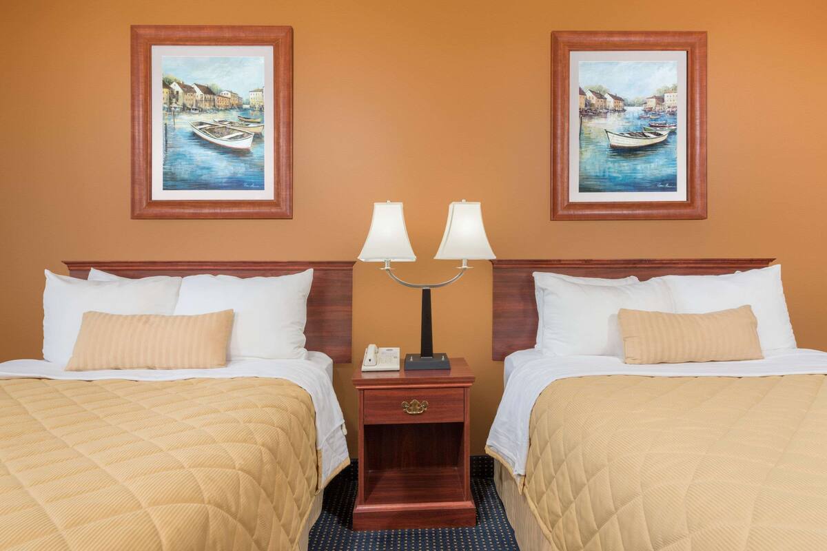 Een hotelkamer met twee bedden, een nachtkastje met een lamp en twee ingelijste schilderijen aan de muur.