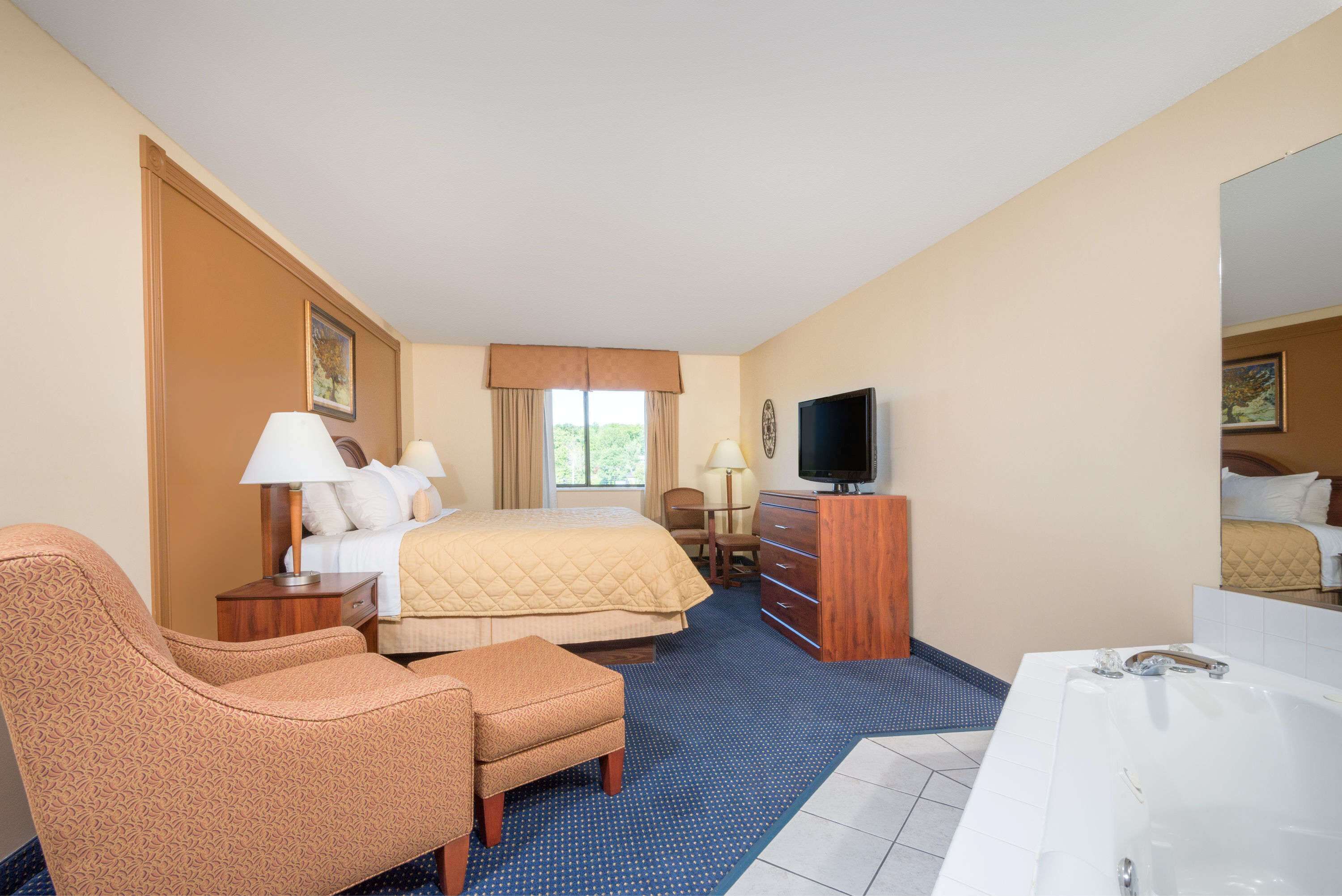 Een hotelkamer met een bed, een bureau met een computer, een stoel, een televisie en een badkamer met een bad.