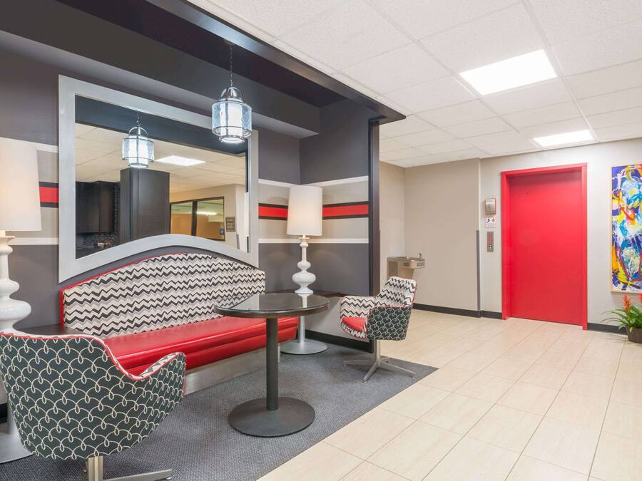 Een moderne lobby met een rode deur, een grote spiegel, een bank, twee gestreepte stoelen en een kleine plant.