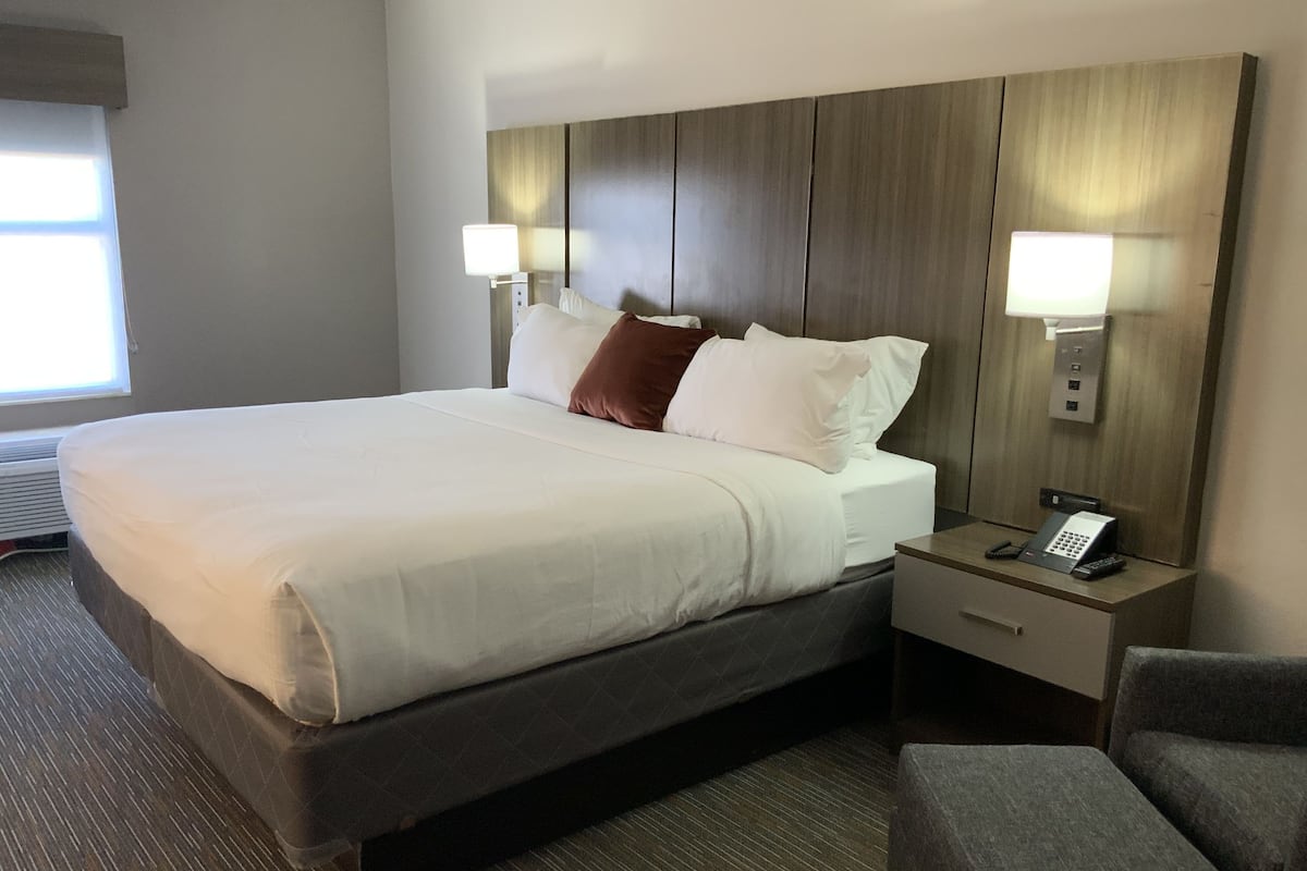 A hotel room with a large bed, bedside lamps, a telephone, and a chair.