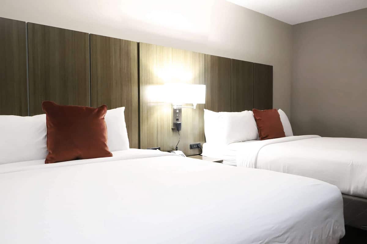 A hotel room with two beds, a wall-mounted lamp, and a wooden panel wall.