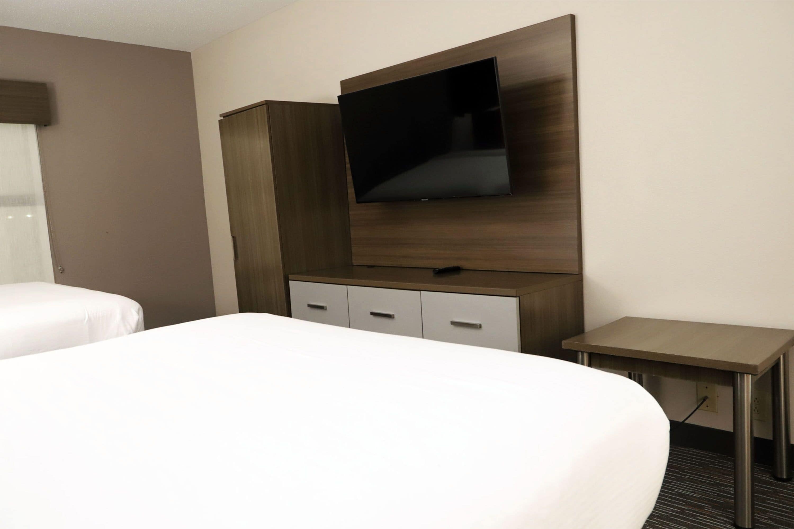 Une chambre d’hôtel comprenant un lit, un téléviseur fixé sur un panneau en bois, un petit bureau et une armoire.