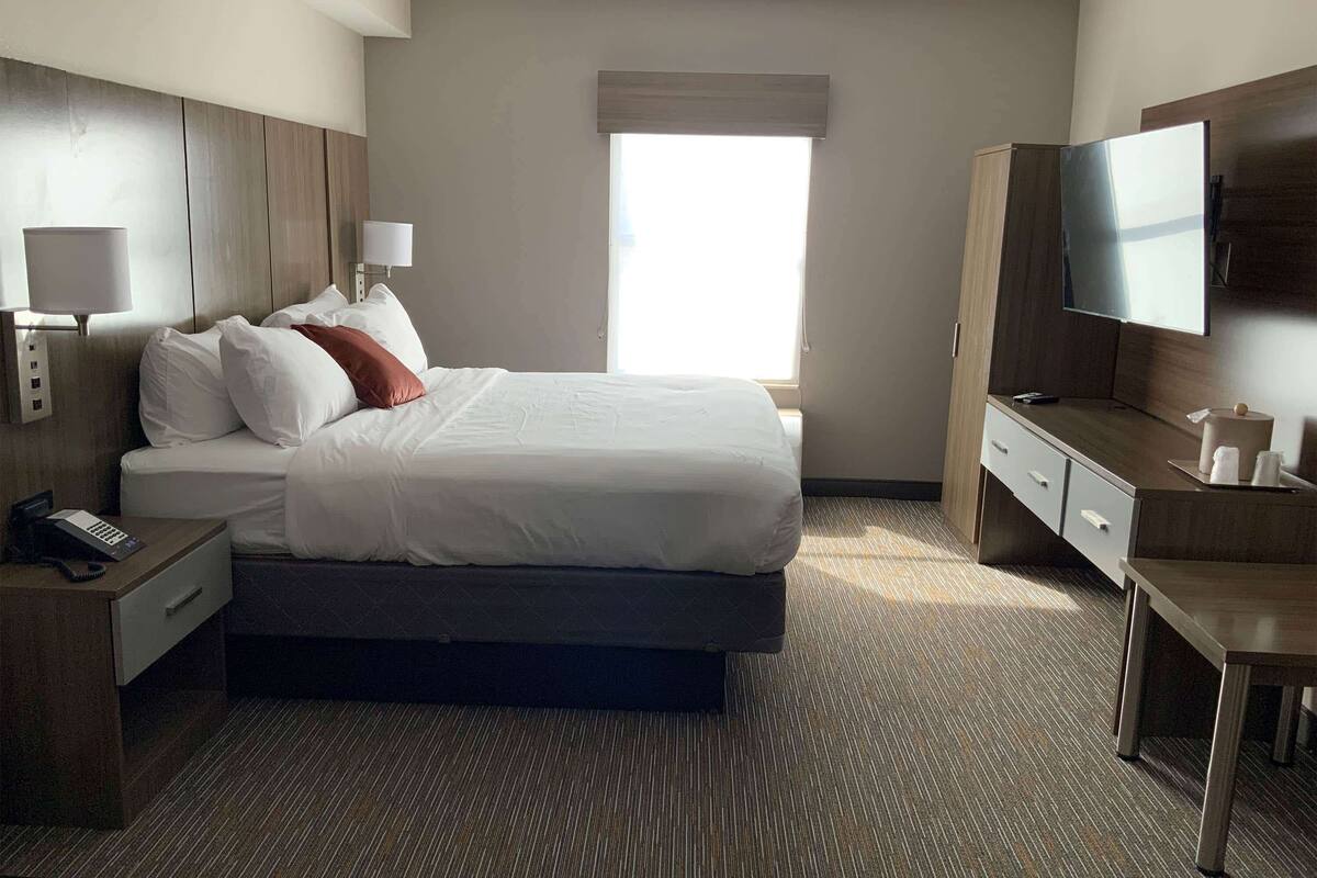 A hotel room with a bed, bedside tables, a desk, a television, and a window.