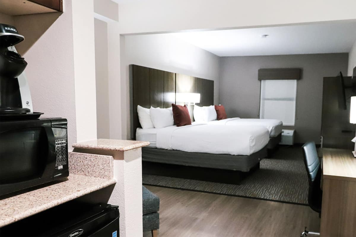 A hotel room with a bed, a desk, a chair, a microwave, and a television.