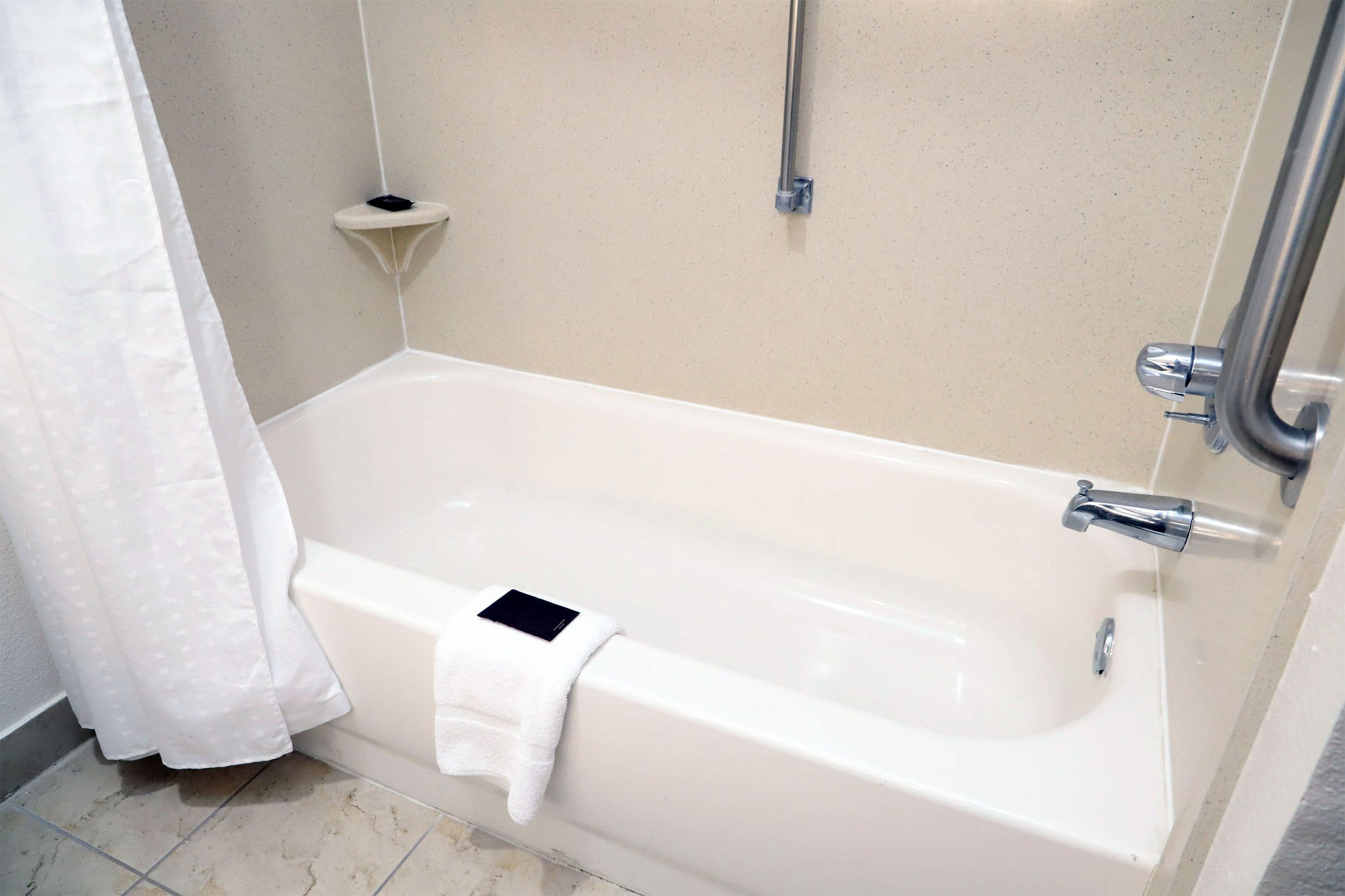 A modern bathroom with a white bathtub, a handheld showerhead, and a small shelf.