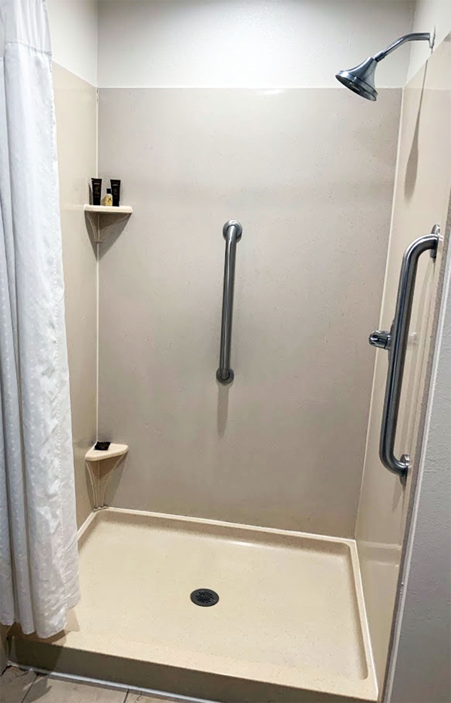 A walk-in shower with a beige floor, a handheld showerhead, and a grab bar.