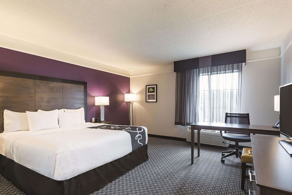 A hotel room with a bed, desk, chair, and a large window with curtains.