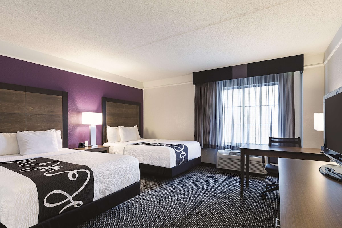A hotel room with two beds, a desk, and a TV.