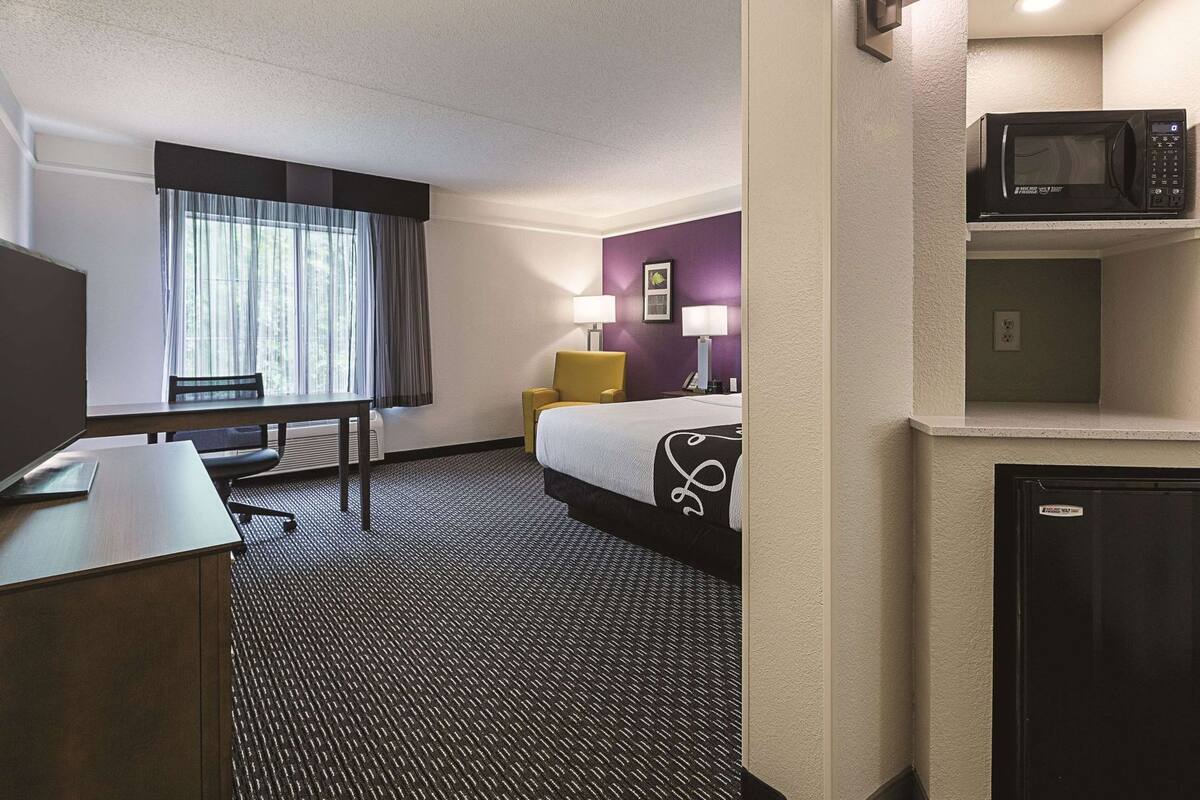 A hotel room with a bed, desk, chair, lamp, and a microwave.