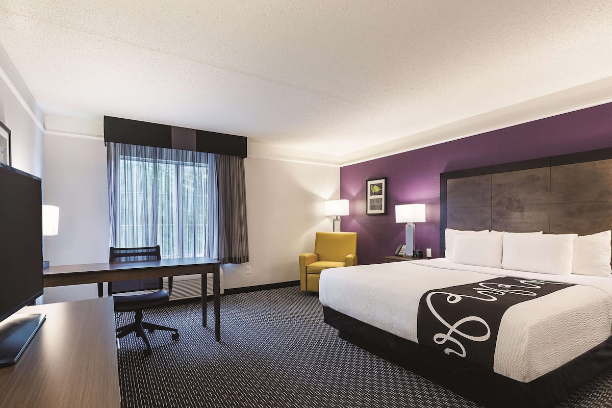 A hotel room with a bed, a desk, a chair, and a window with curtains.