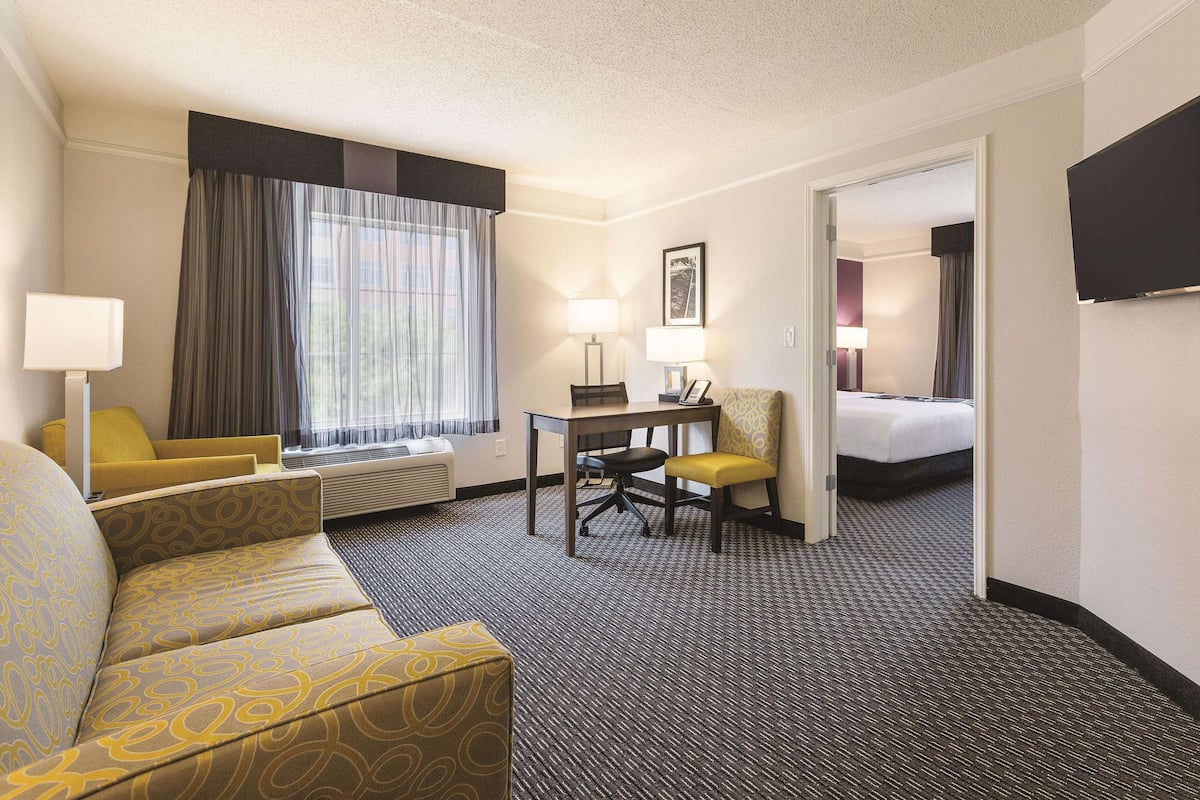 A hotel room with a sofa, a desk, a chair, a bed, and a TV.