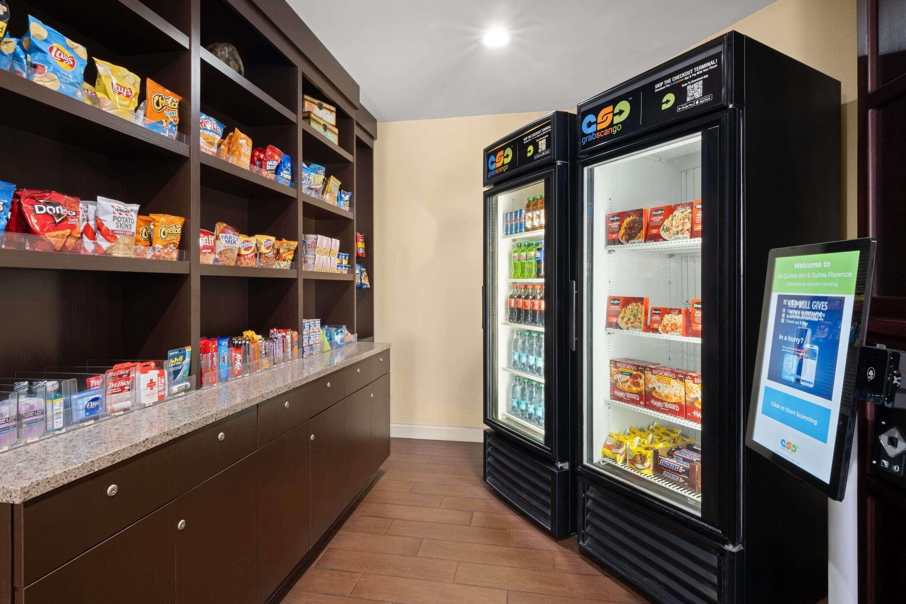 Un mostrador con estantes llenos de papas fritas y diversos bocadillos, y dos vitrinas refrigeradas con bebidas y alimentos.