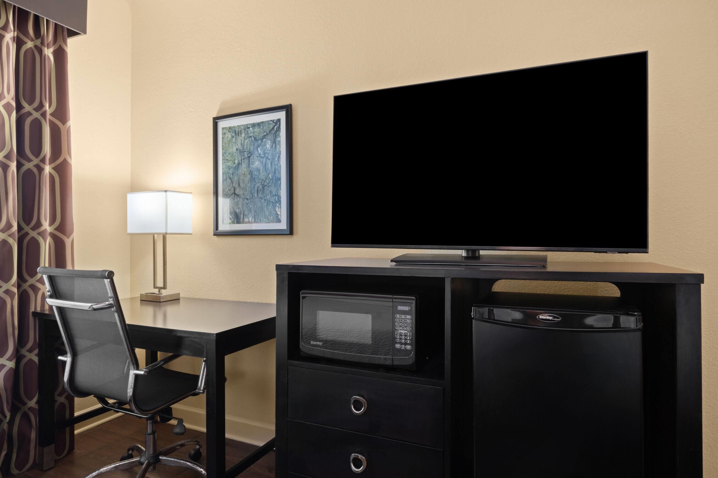 Habitación de hotel con escritorio, silla, televisión de pantalla plana, microondas y refrigerador pequeño.
