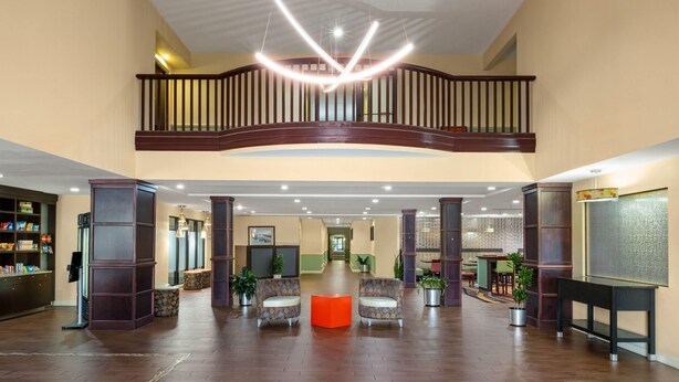 A spacious lobby with a high ceiling, a central seating area, and a staircase leading to an upper level. - La Quinta Inn & Suites by Wyndham Florence (Florence)