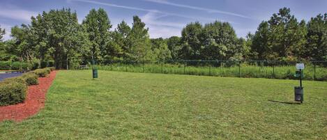 A grassy outdoor area with a fence, trees, and a signpost.