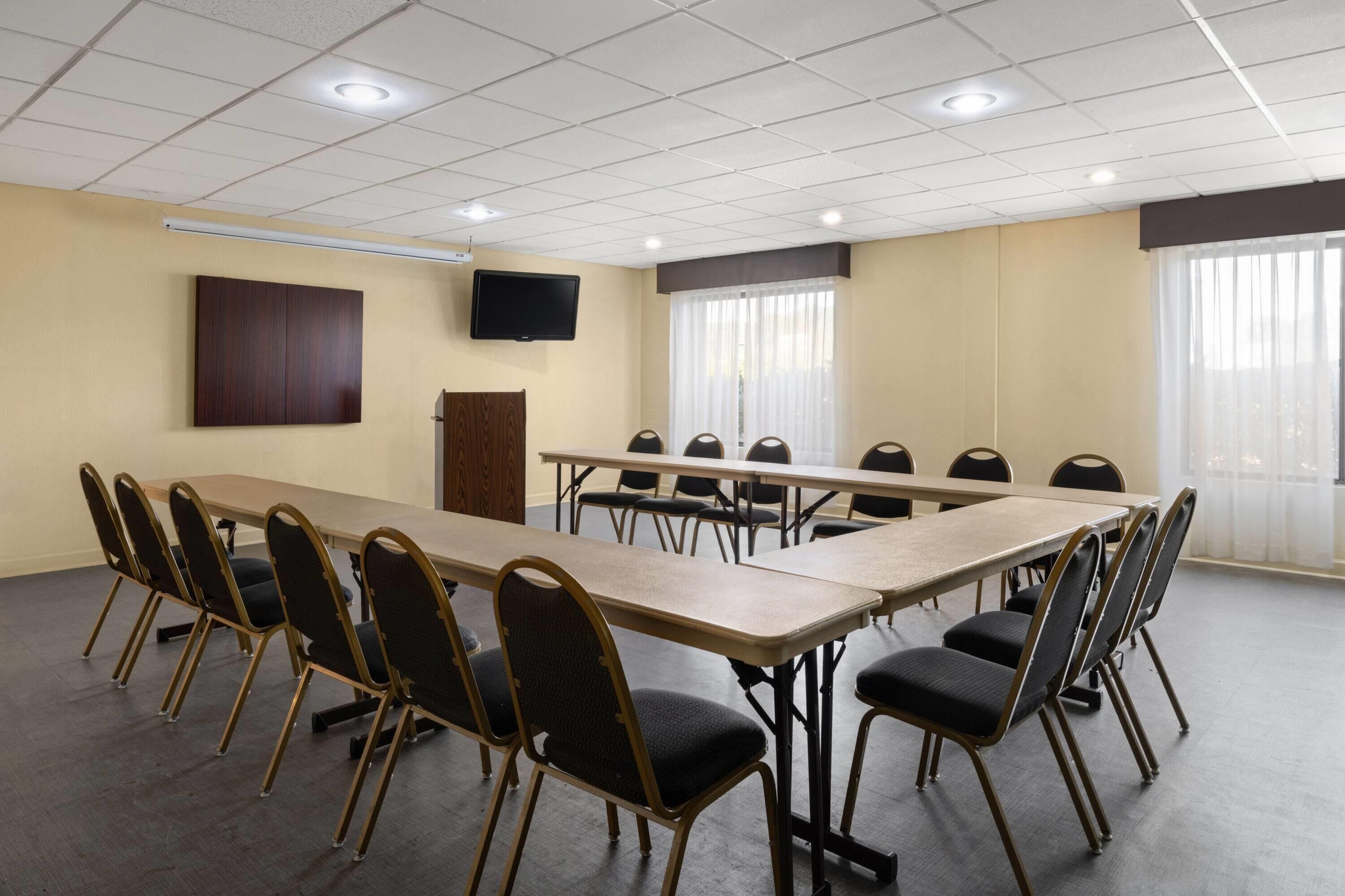Un salón de conferencias con una larga mesa y sillas, un televisor de pantalla plana y ventanas amplias con cortinas.