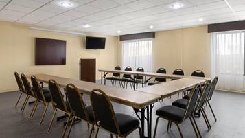 Un salón de conferencias con una larga mesa y sillas, un televisor de pantalla plana y ventanas amplias con cortinas.