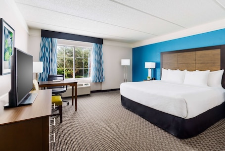 A hotel room with a large bed, a desk with a computer, a TV, and a window with curtains.