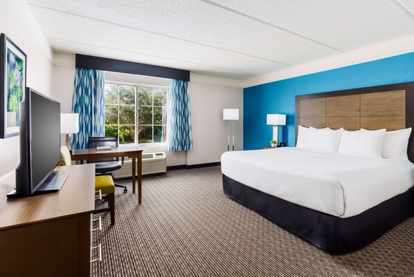 Habitación de hotel con una cama grande, un escritorio con computadora, un televisor y una ventana con cortinas.