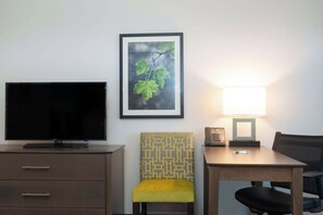 A hotel room with a flat-screen TV, a framed picture of a leaf, a lamp, a chair, and a desk. - La Quinta Inn & Suites by Wyndham Tampa Brandon Regency Park (Brandon)