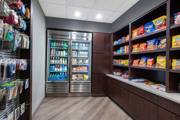 A self-service snack and beverage area with refrigerated drink dispensers and shelves stocked with various snacks and packaged goods. - La Quinta Inn & Suites by Wyndham Tampa Brandon Regency Park (Brandon)