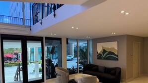 Eine moderne Lobby mit Glastür, einer schwarzen Ledersofa, grauen Fußhocker und einem großen abstrakten Gemälde an der Wand.