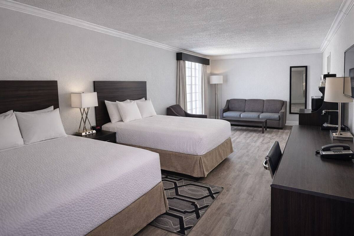 Ein Hotelzimmer mit zwei Betten, einem Schreibtisch, einem Sessel, einer Couch und einem großen Spiegel.