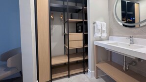 Ein modernes Badezimmer mit integriertem Waschtisch, einem Spiegel und einem begehbaren Kleiderschrank mit Regalen und Ablagefläche.