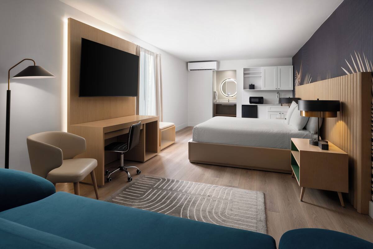 Ein modernes Hotelzimmer mit einem großen Bett, einem Schreibtisch, einem Fernseher, einer Küchenzeile und einer Sitzecke.