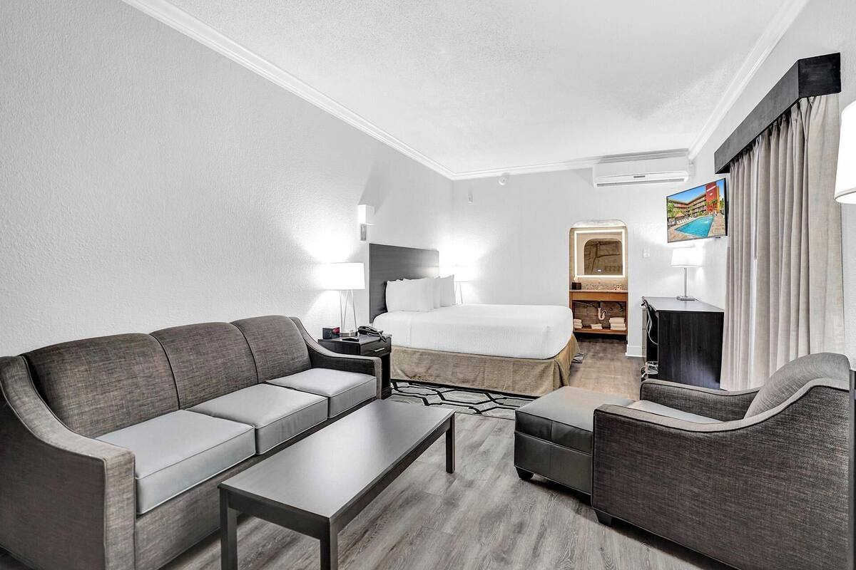Ein Hotelzimmer mit einer Couch, einem Bett, einem Schreibtisch, einem Fernseher und einem Badezimmer.