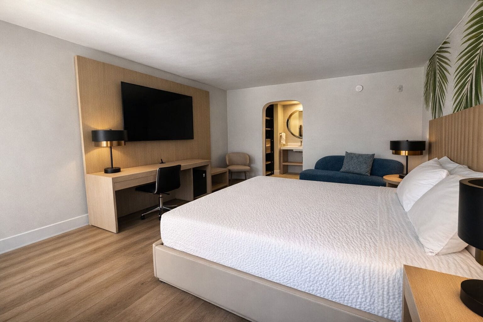 Moderni hotellihuone, jossa on suuri sänky, työpöytä tuolilla, seinälle asennettu televisio ja peilillä varustettu vaatekaappi.