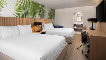 A hotel room with two beds, a desk, a chair, a TV, and a bathroom with a mirror.