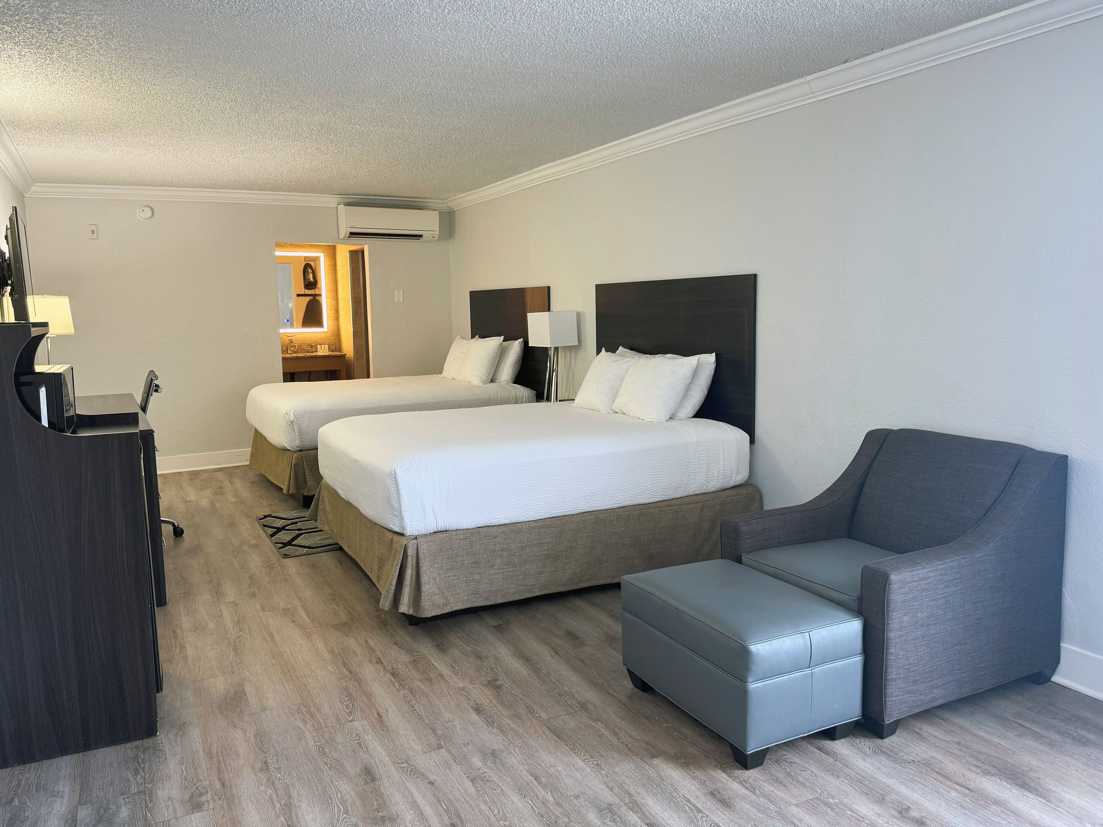 A hotel room with two beds, a desk, a chair, and a small ottoman.