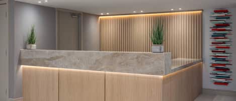 Mostrador de recepción con encimera de mármol, paneles de madera e iluminación empotrada. Hay dos plantas en macetas sobre el mostrador.