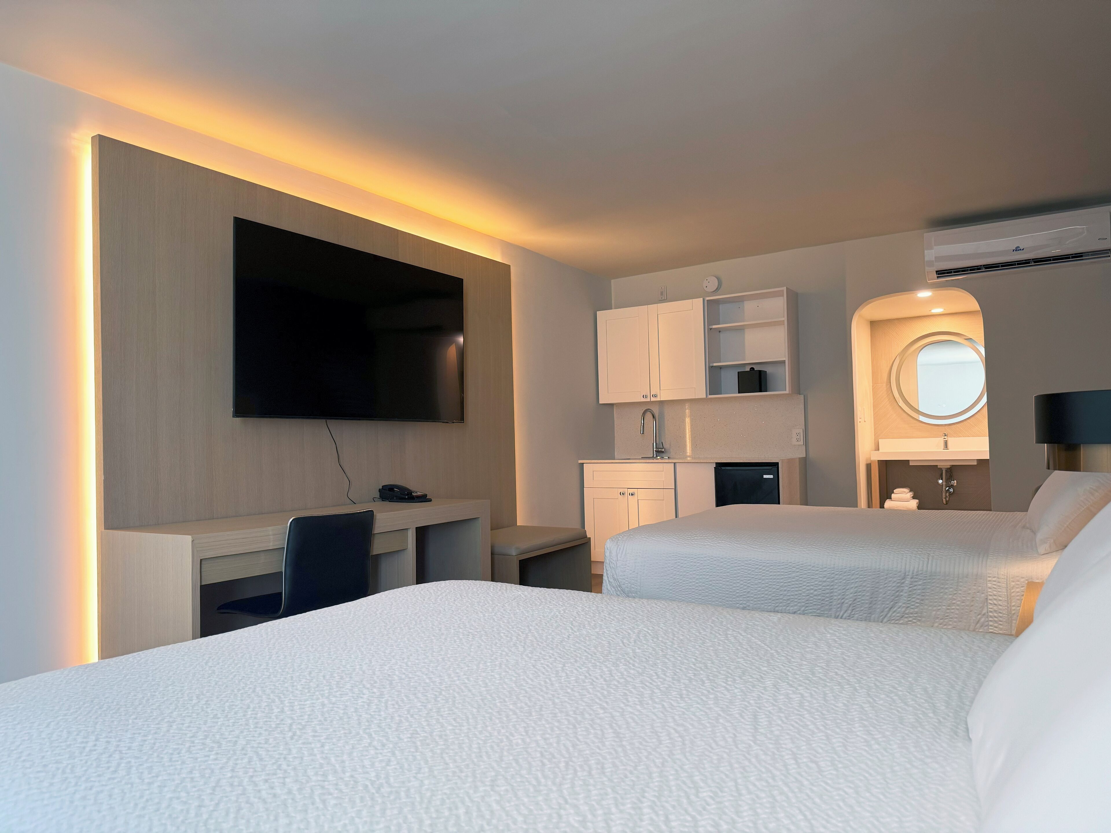 A hotel room with a bed, a desk, a TV, a small kitchenette, and a bathroom.