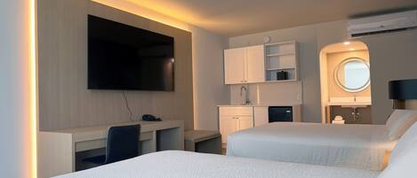Une chambre d’hôtel comprenant un lit, un bureau, une télévision, une petite kitchenette et une salle de bain.
