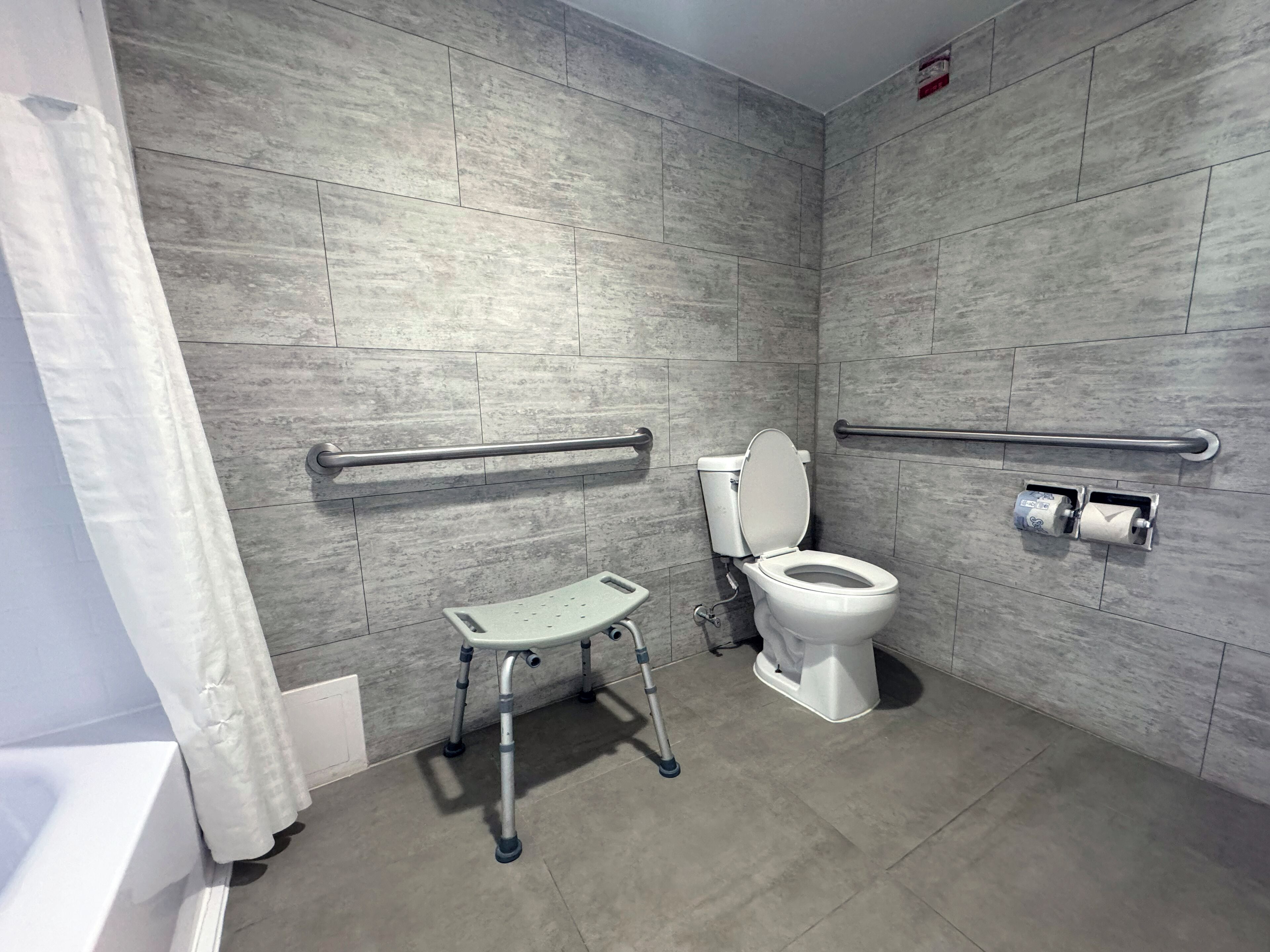 Un baño moderno con inodoro accesible para sillas de ruedas, barras de apoyo y asiento de ducha.