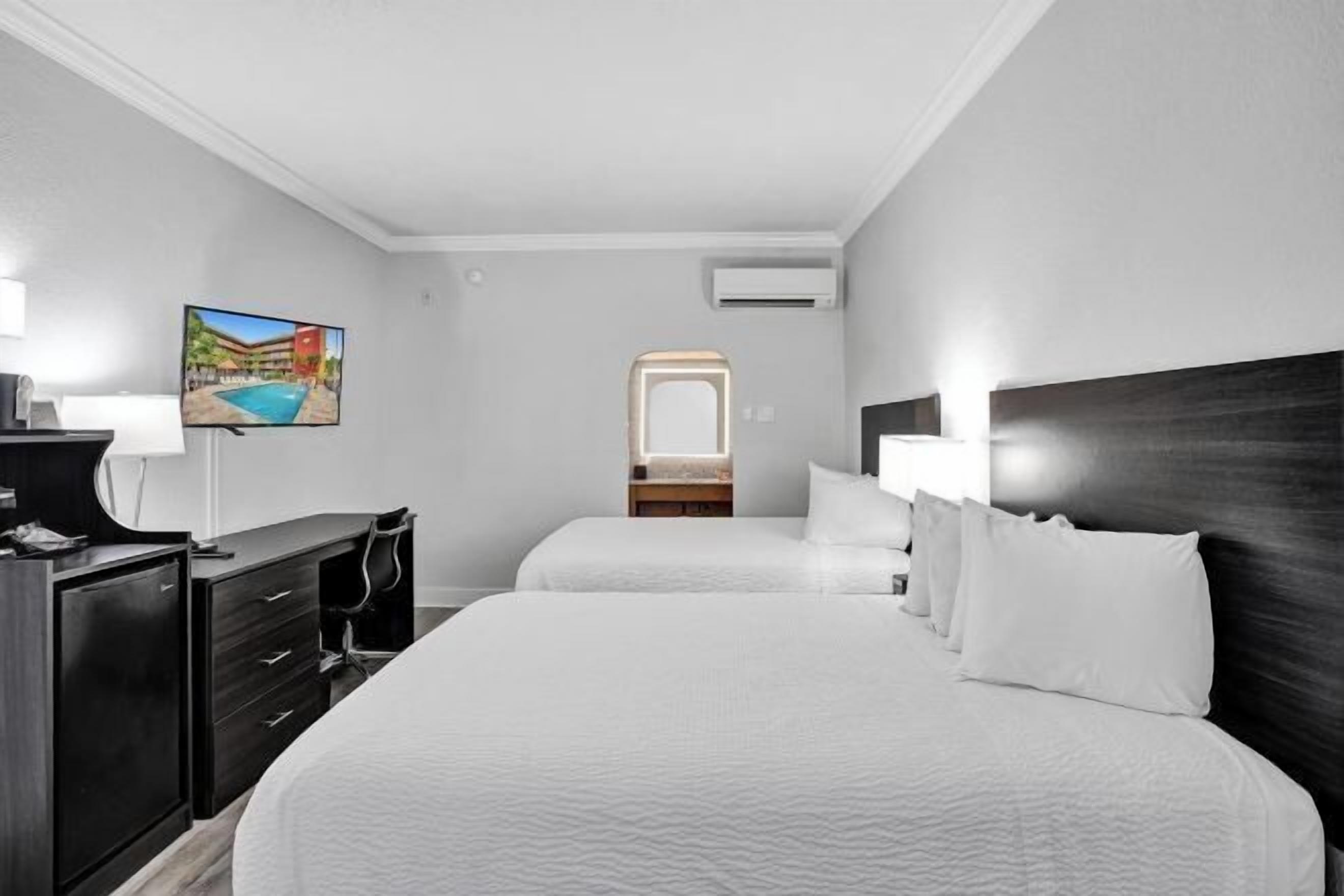 Ein Hotelzimmer mit zwei Betten, einem Fernseher, einem Schminktisch und einem Spiegel.