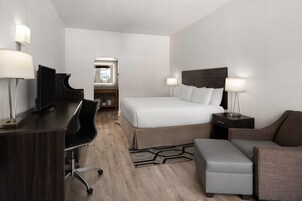 A hotel room with a bed, a desk with a chair, a small sofa, a nightstand, and a lamp.