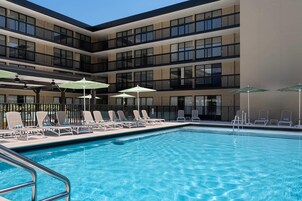 A swimming pool with lounge chairs and umbrellas, surrounded by a multi-story building with balconies.