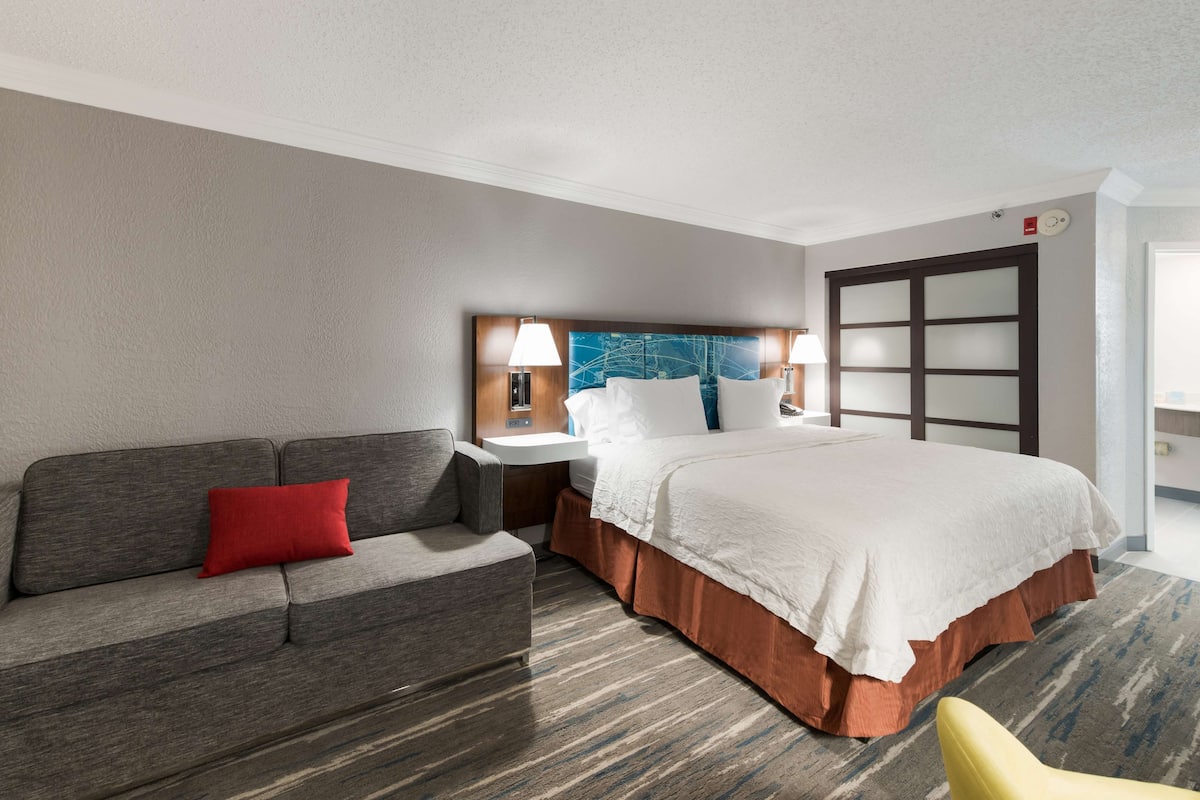 A hotel room with a bed, a sofa, a nightstand, and a chair.