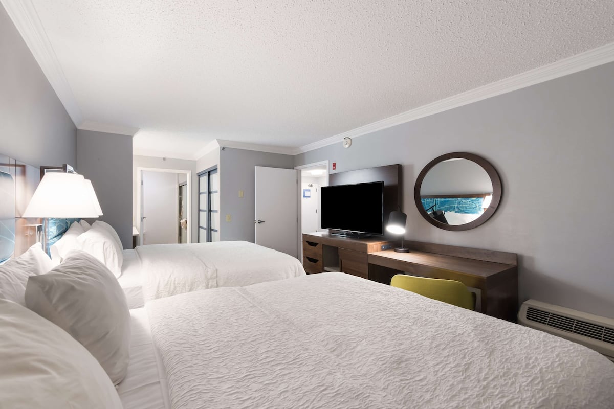 A hotel room with two beds, a desk with a computer, a TV, and a mirror.
