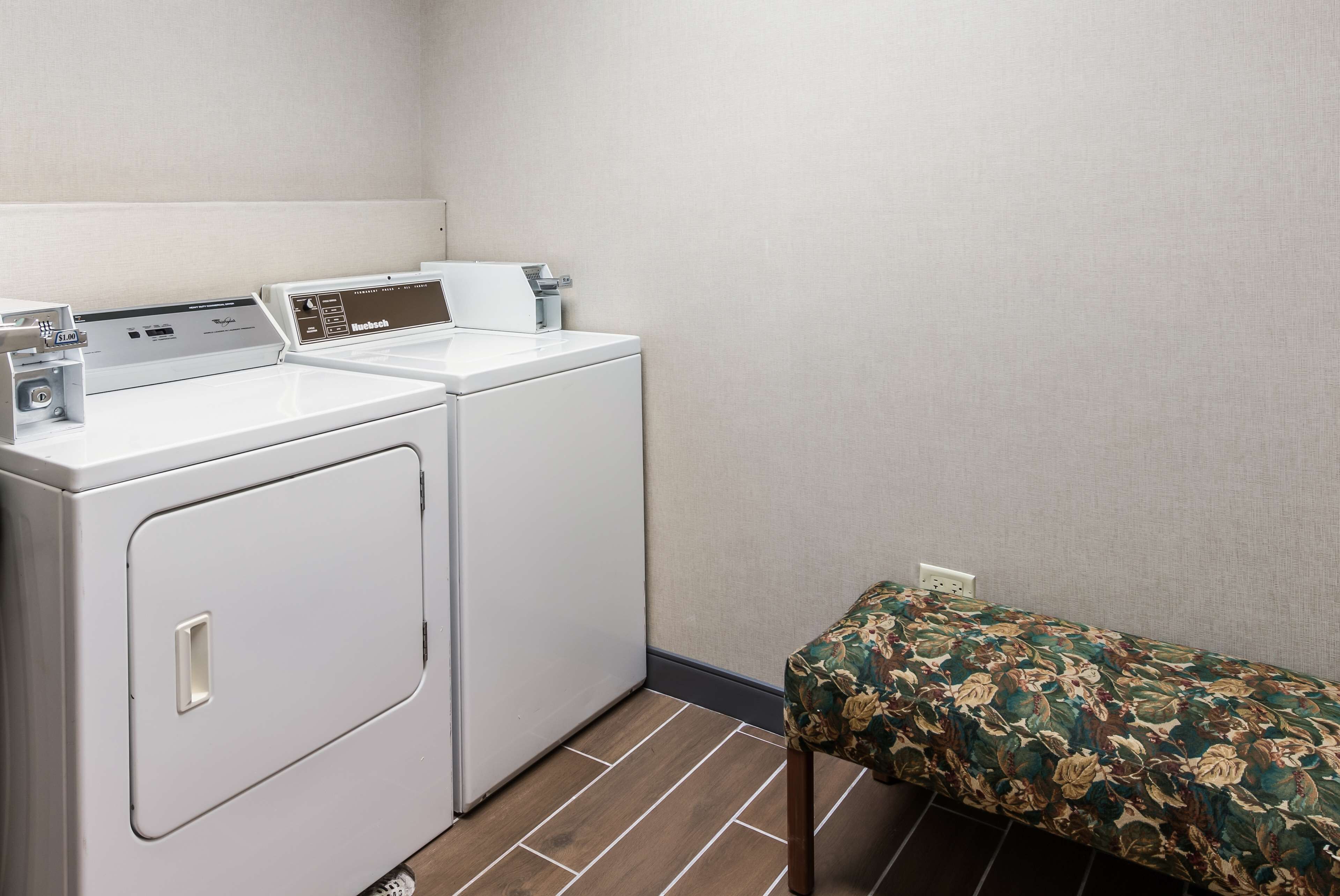 A laundry area with two white washing machines and a bench with a floral cover.