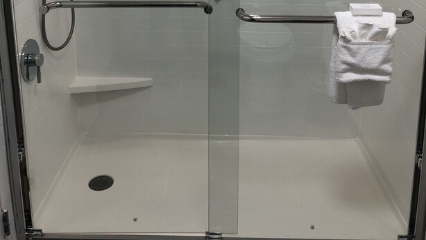 A glass-enclosed shower with a handheld showerhead, a handheld shower attachment, and a towel rack with a white towel. - Hampton Inn & Suites Chicago/Hoffman Estates (Hoffman Estates)