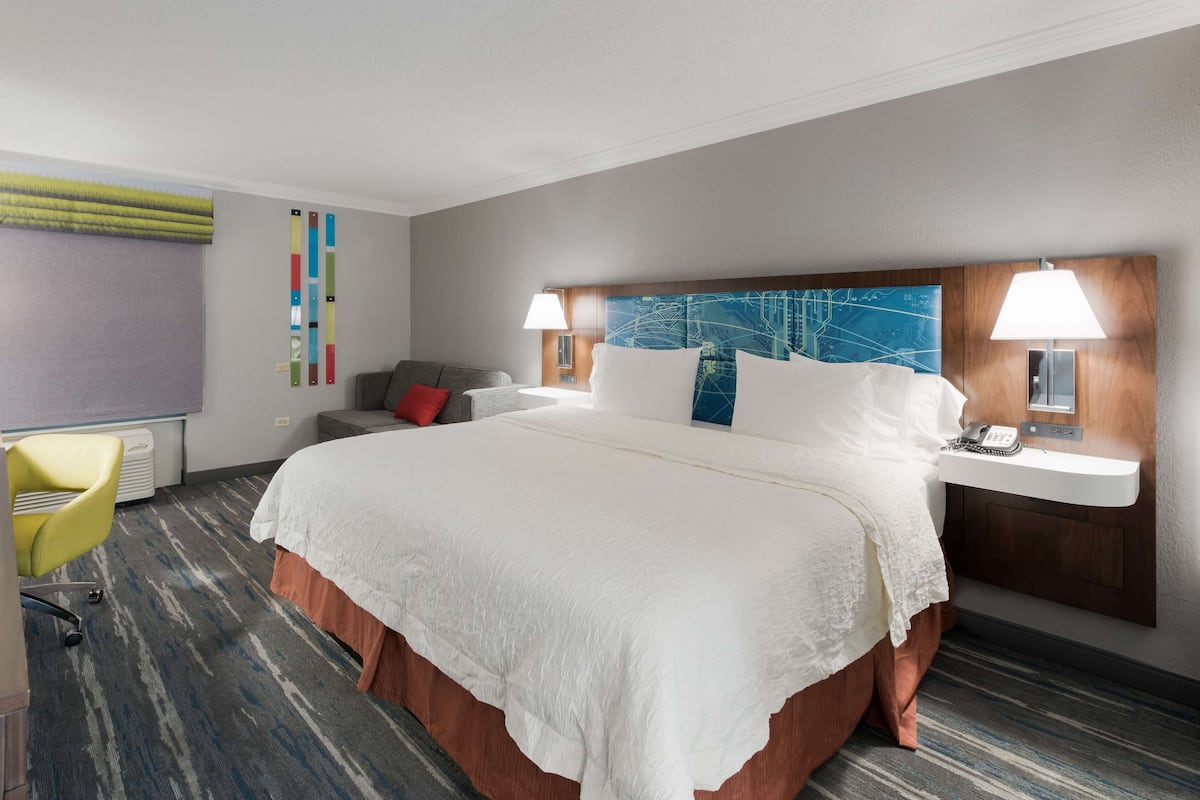 A hotel room with a large bed, a desk with a chair, a small table, and a map on the wall.