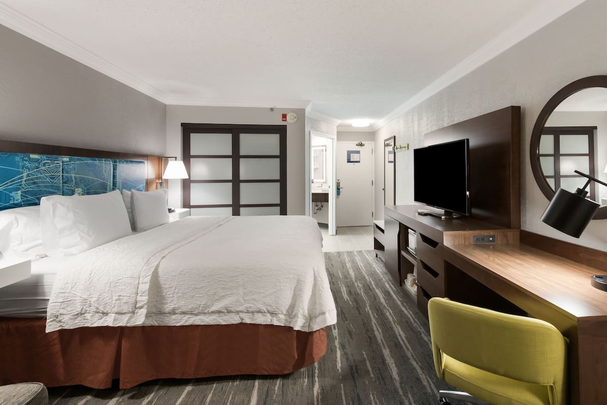 A hotel room with a large bed, a desk with a television, a chair, and a map on the wall.