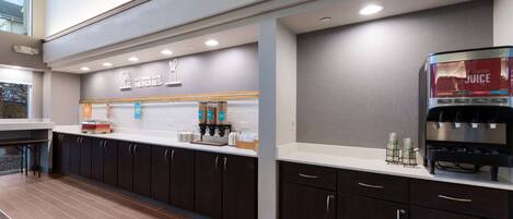 A modern kitchen area with a coffee station, a juice dispenser, and a countertop with various items.