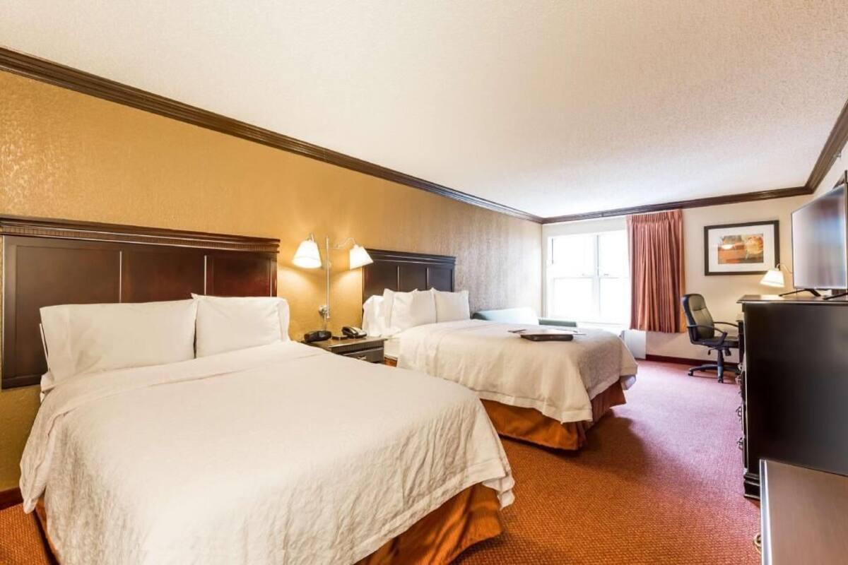 A hotel room with two beds, a desk, a chair, and a television.